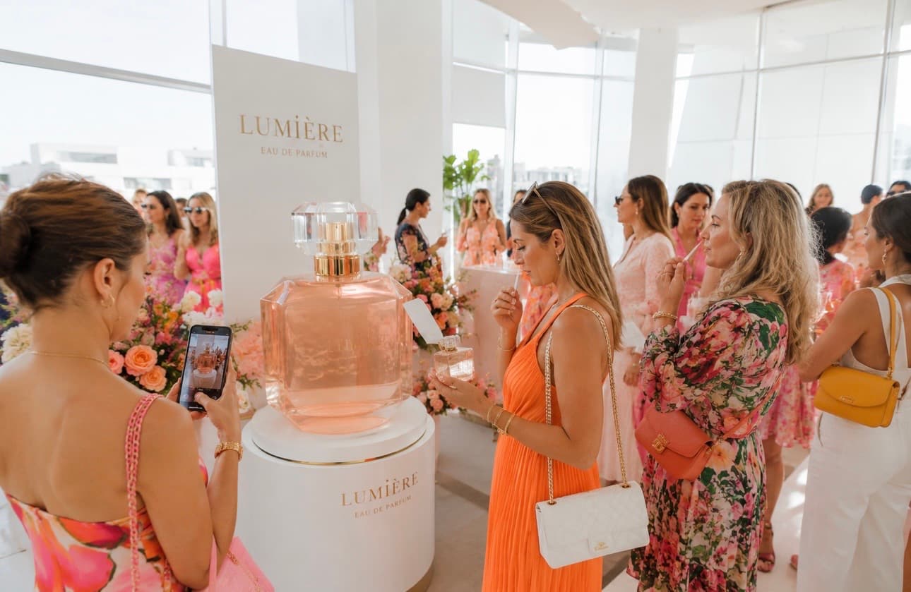 Frauen bestaunen bei einer Produktpräsentation den überdimensionalen Flakon „Lumière Eau de Parfum“, eine fotografiert ihn mit dem Handy