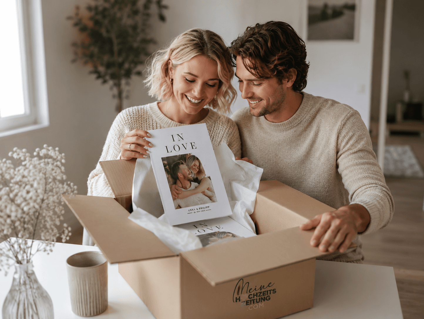 Ein junges Paar packt aus einem Karton von Meine Hochzeitszeitung ein Magazin mit dem Titel „In Love“ aus.