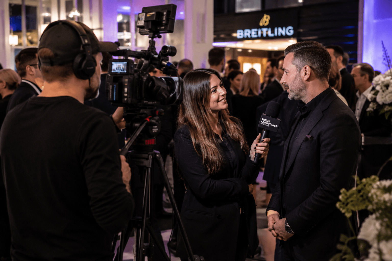 Interview bei einem Event: Eine Frau hält einem Mann ein Mikrofon mit Weiss-Lameraner-Logo hin, links filmt ein Kameramann.