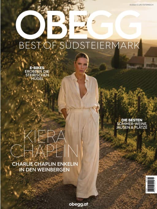 Cover von OBEGG – Best of Südsteiermark: Frau in Cremetönen auf einem Weg zwischen Olivenzweigen und Weinreben, Titelthema Kiera Chaplin