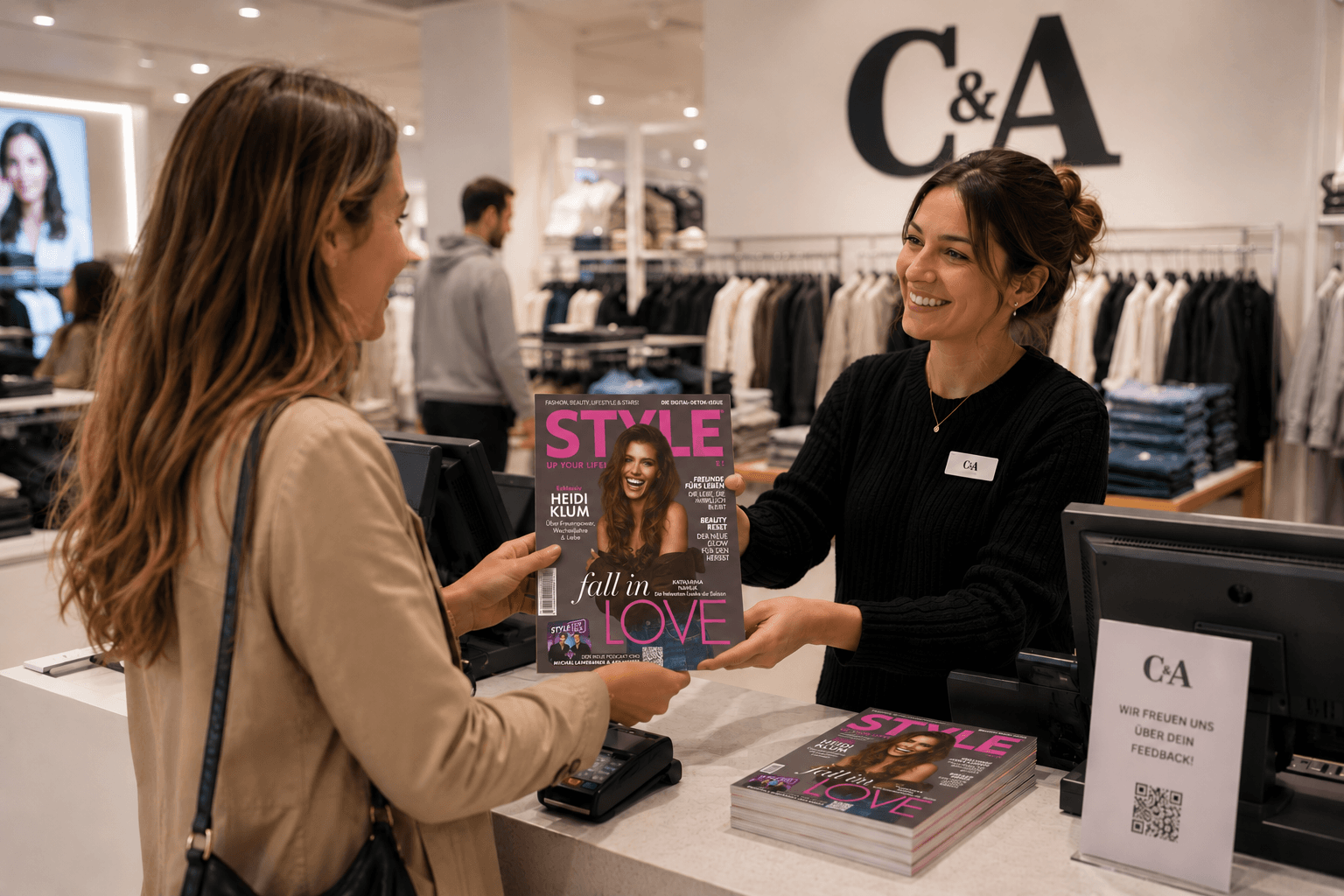 Verkäuferin und Kundin halten an einer C&A-Kasse ein Heft von STYLE UP YOUR LIFE!, auf dem Tresen liegt ein Stapel weiterer Hefte.